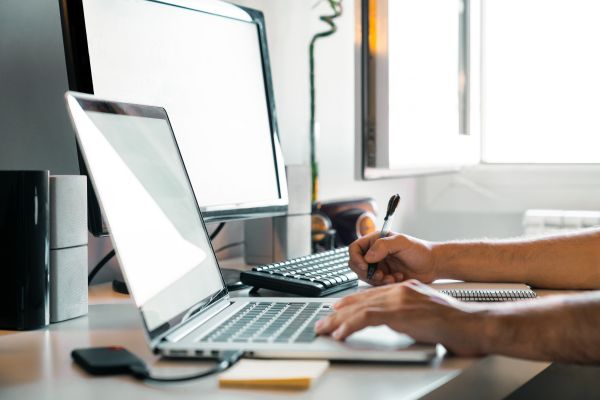Hände einer Person an Bildschirm und Laptop