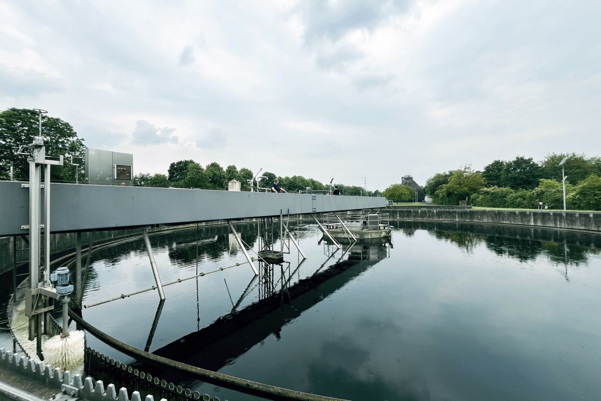 Klärbecken mit Räumer und Himmelspiegelung im Wasser